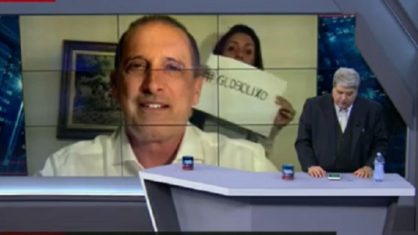 Mulher exibe cartaz ‘Globo lixo’ durante entrevista de ministro a Datena